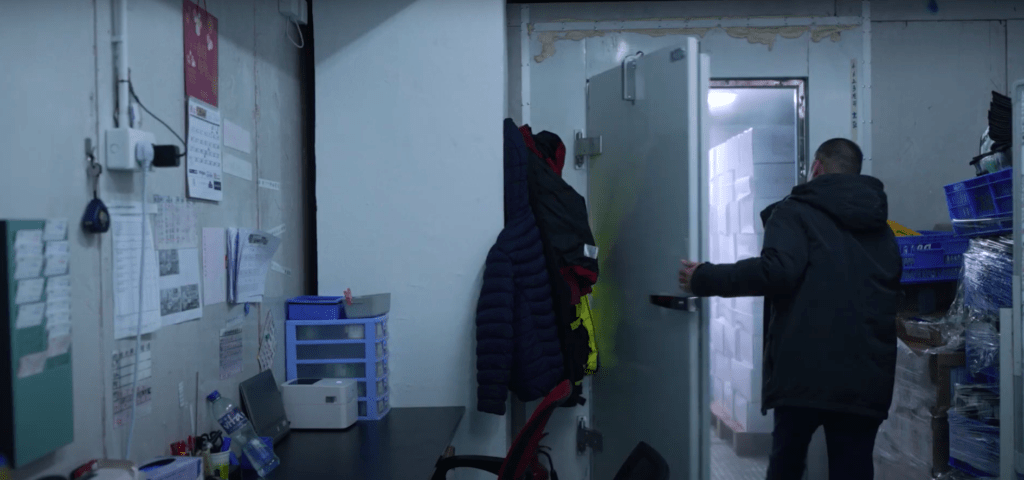 一个男人站在中小企业办公室里，面向门口，周围摆放着简单的家具，灯光温暖。